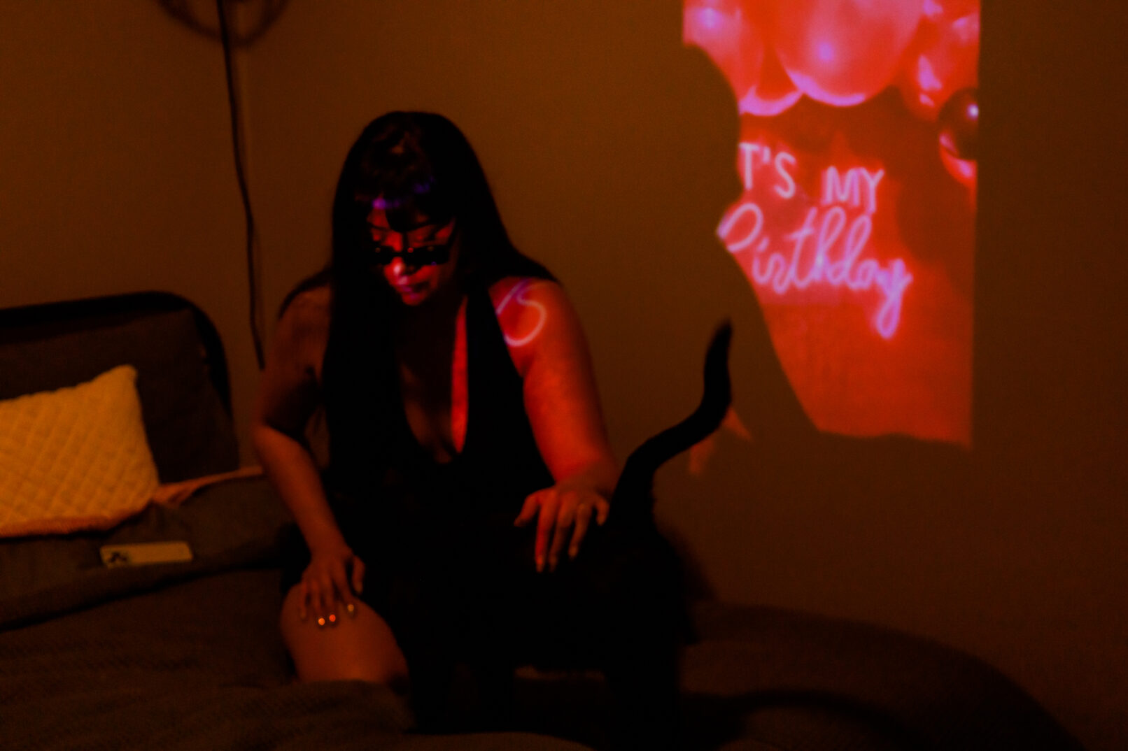 a woman sitting on her bed by a pink light, petting a black cat