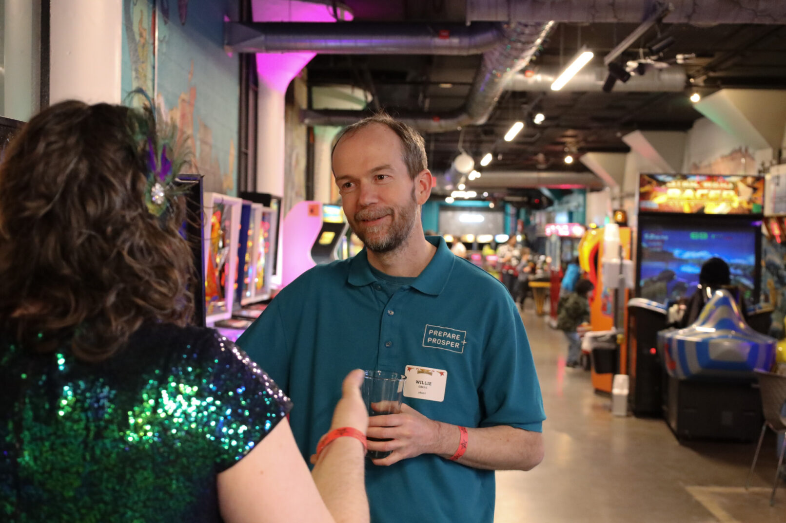 a man in a blue tshirt standing in an arcade talking to a woman in a green dress