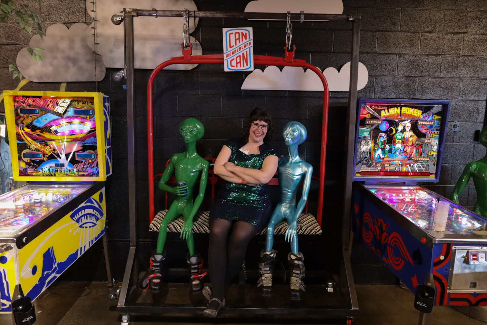 woman in a green dress sitting on a swing between two aliens